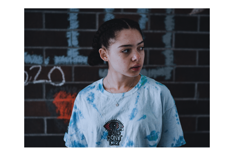 Model wearing a blue tie-dye graphic tee with a screen printed chest graphic against a brick wall