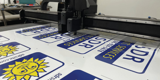 Flatbed cutting table trimming printed blue and yellow SDR site services sign panels