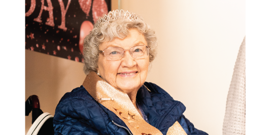 Smiling woman wearing a tiara and birthday sash photographed in warm indoor light