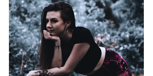 Editorial portrait of a woman resting on her hand outdoors against muted winter foliage