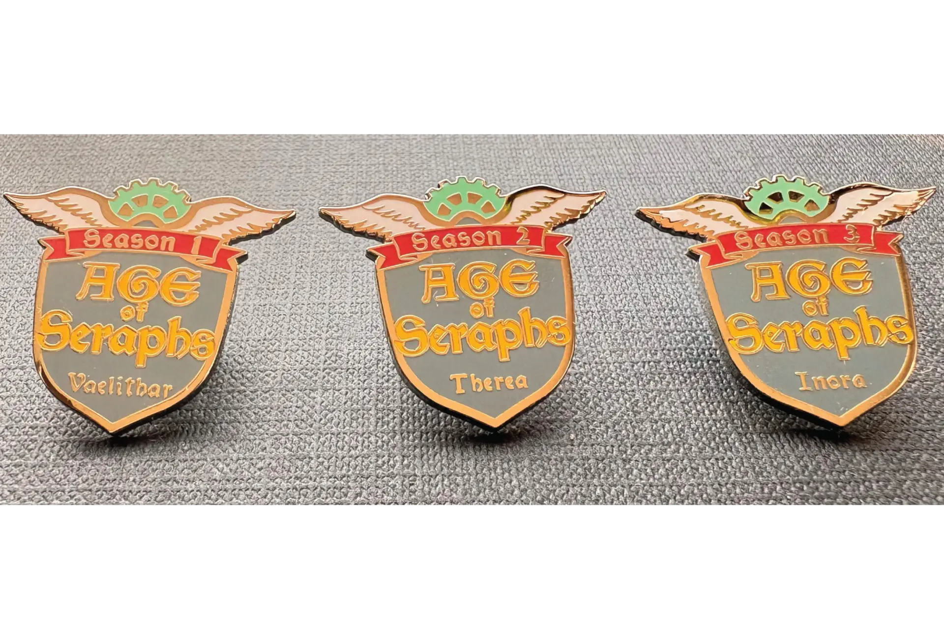 Three gold-plated hard enamel Age of Seraphs collector pins for seasons one, two, and three