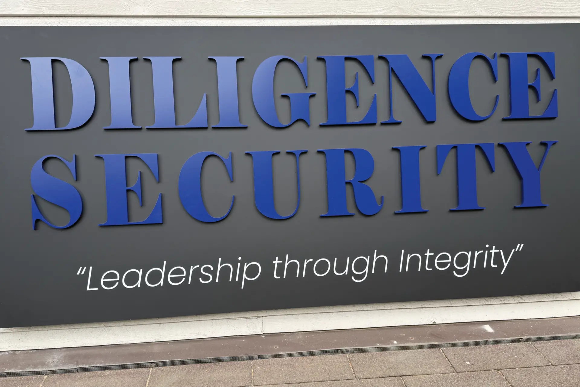 Dimensional blue lettering reading Diligence Security mounted on a dark exterior sign panel