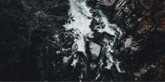 Aerial photograph looking down at whitewater rushing between dark rocks and forest