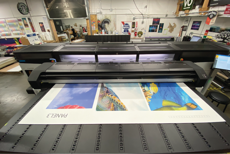 Large-format flatbed printer producing a multi-panel color wall graphic in a production shop