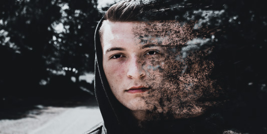 Portrait of a young man with a stylized dispersion effect compositing part of his face into particles