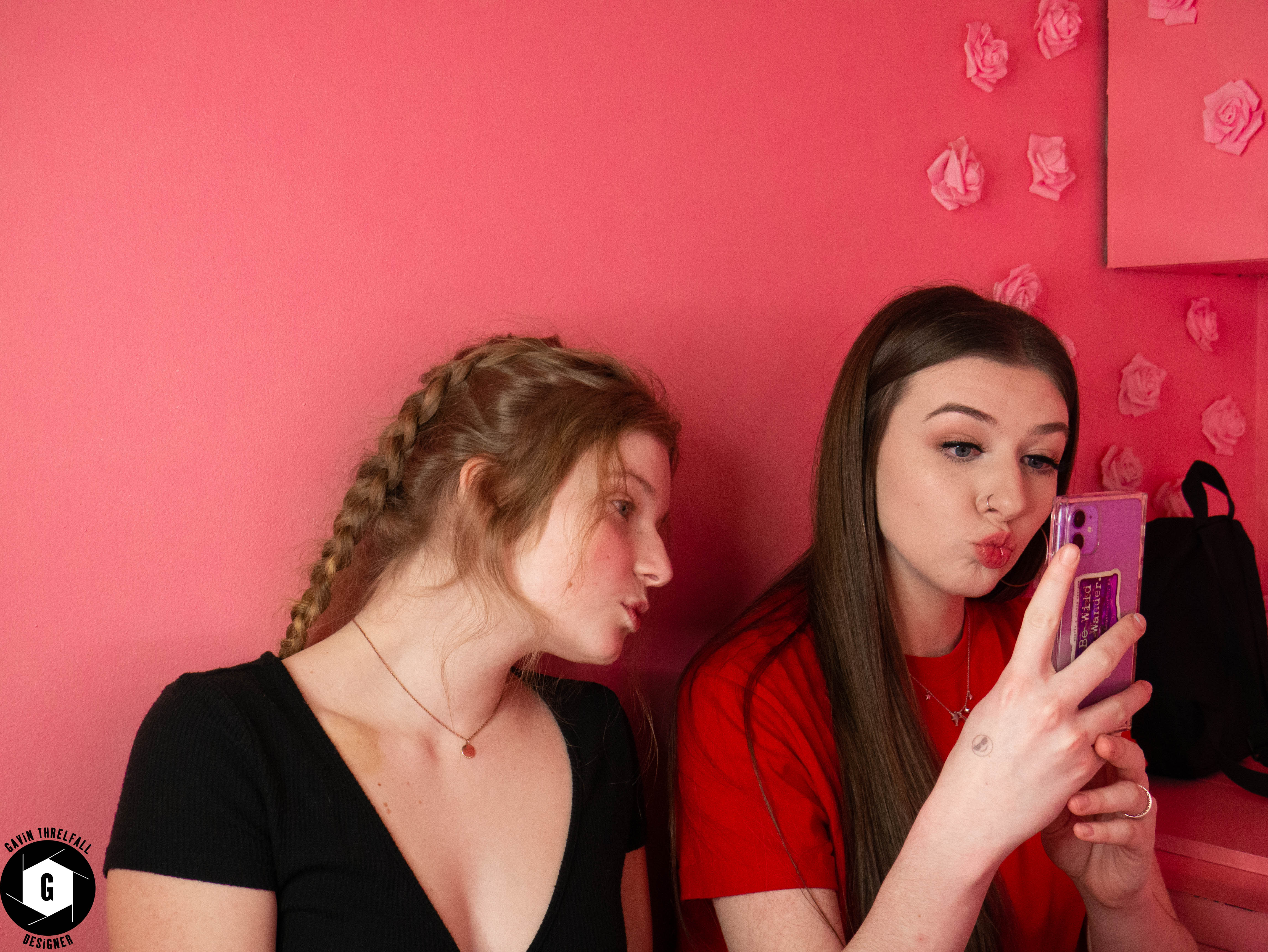Two friends posing against a pink studio wall with a phone