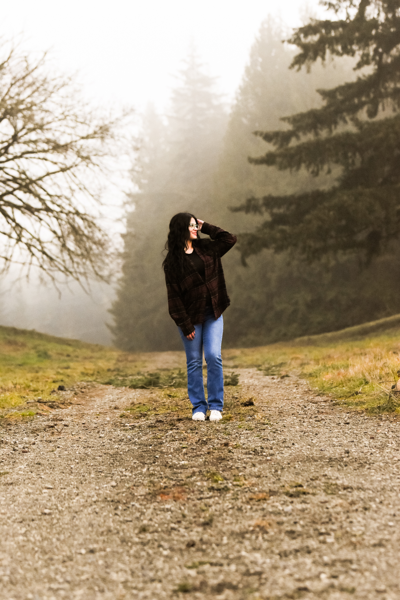 Senior standing on a gravel trail surrounded by fog and evergreens