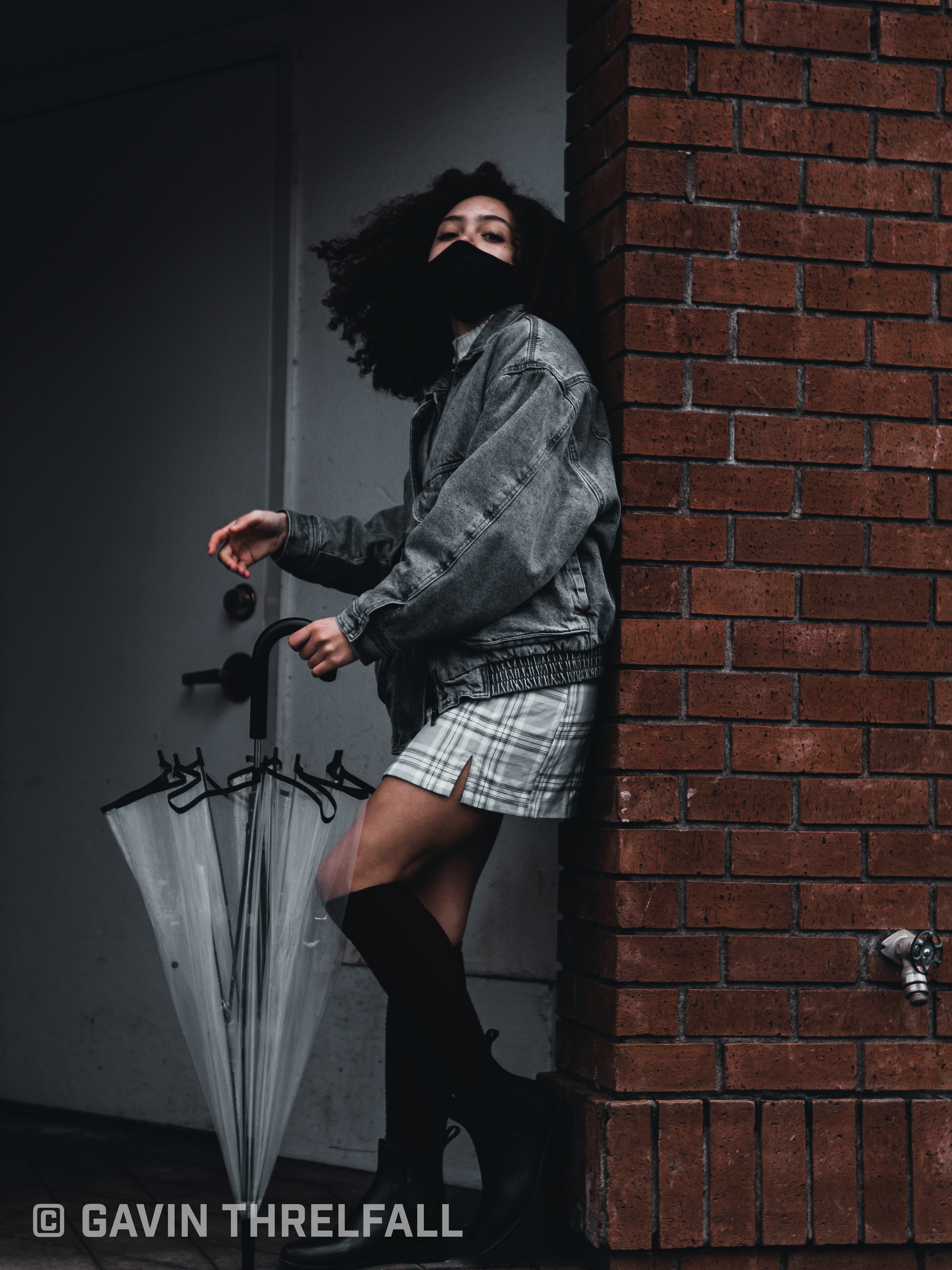 Model posing in a brick doorway holding a folded umbrella