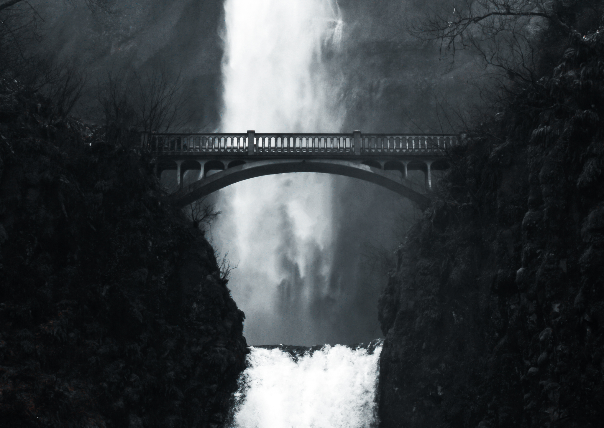 Black and white long exposure of a waterfall and arched bridge in the forest
