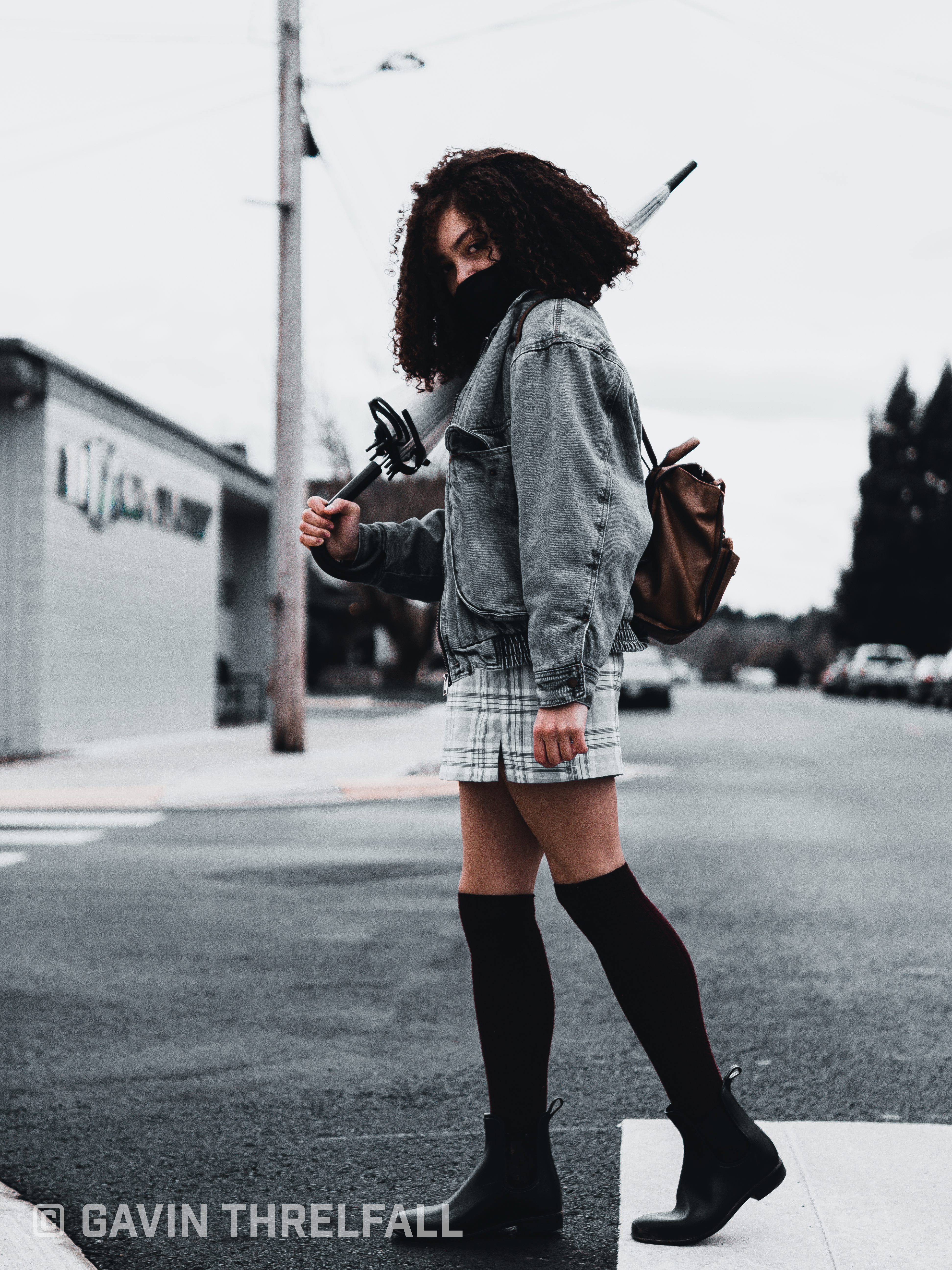 Model striding across a downtown crosswalk with an umbrella