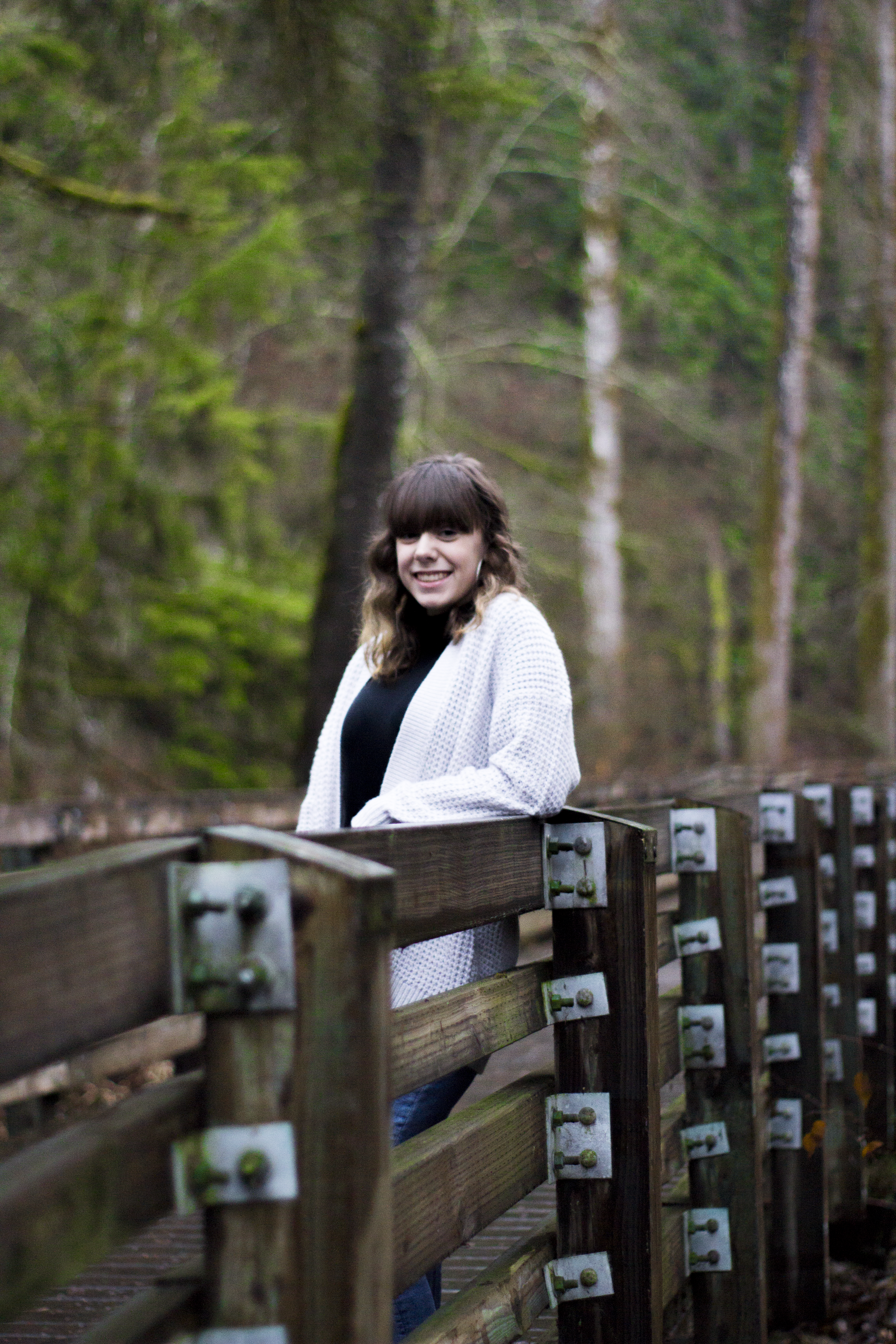 High school senior leaning on a wooden boardwalk railing in the woods