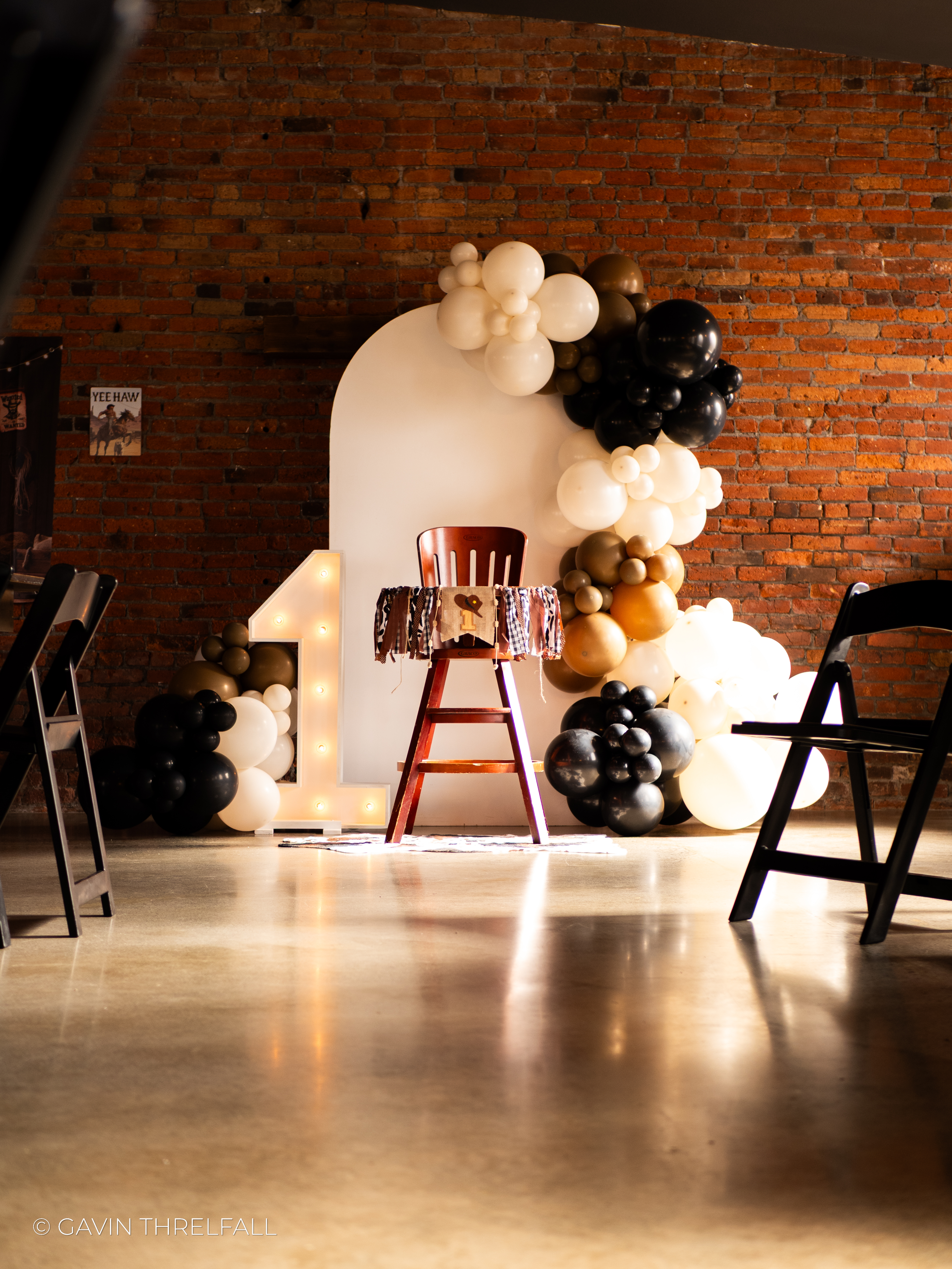 Balloon arch and highchair set up against a brick studio wall