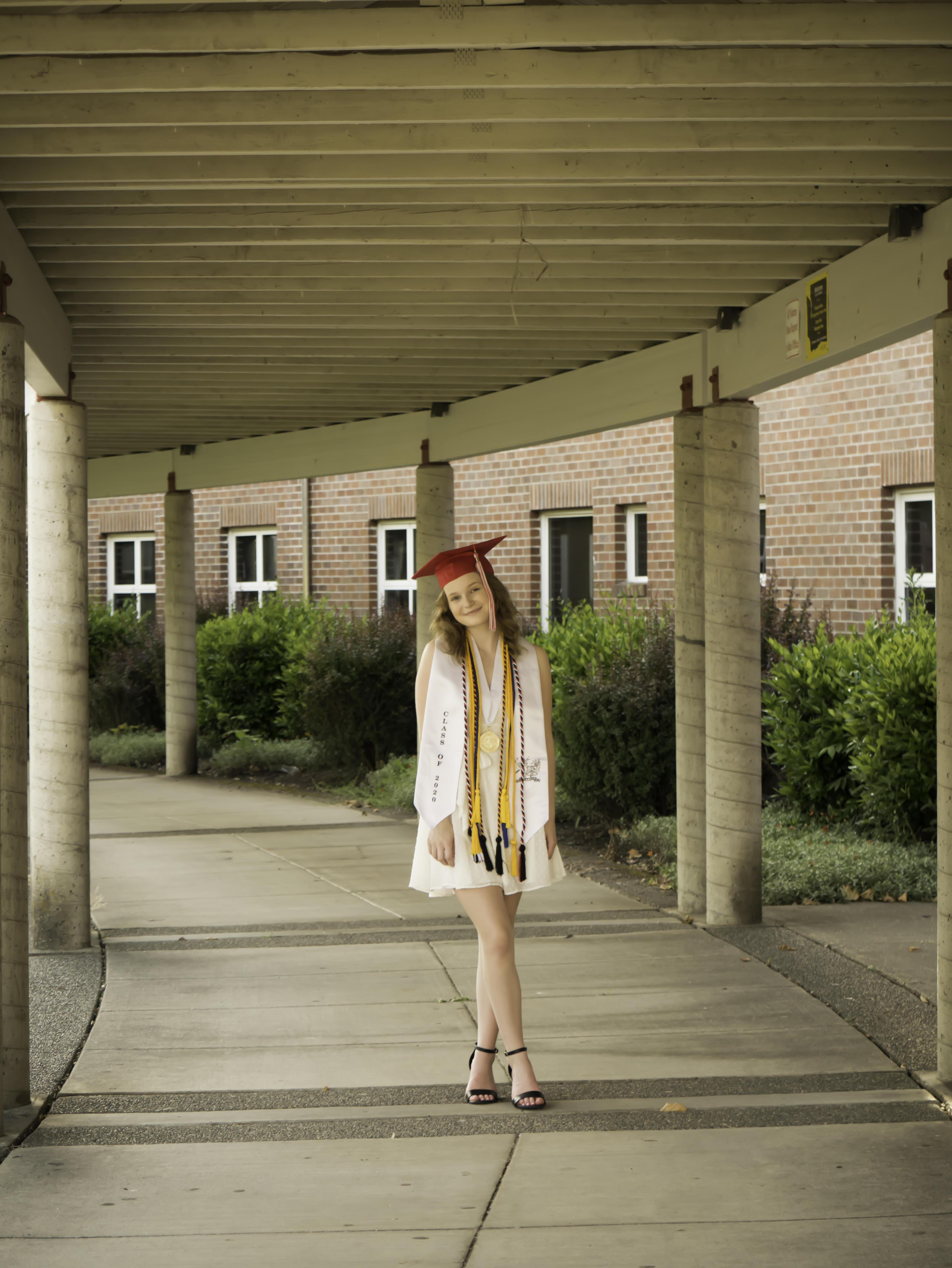 Graduate in cap and gown standing beneath a long campus colonnade