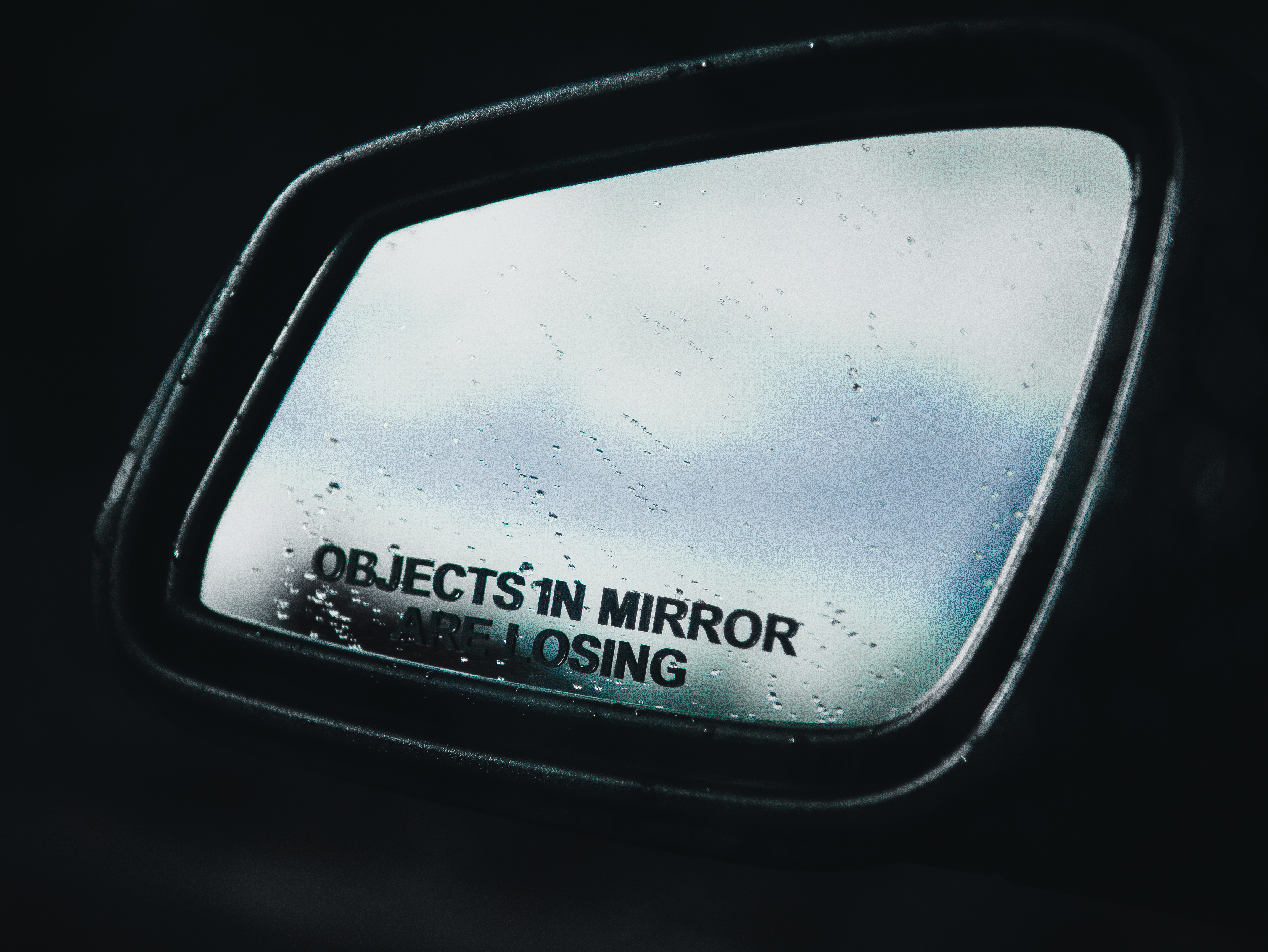 Side mirror of a car with rain drops and the phrase objects in mirror