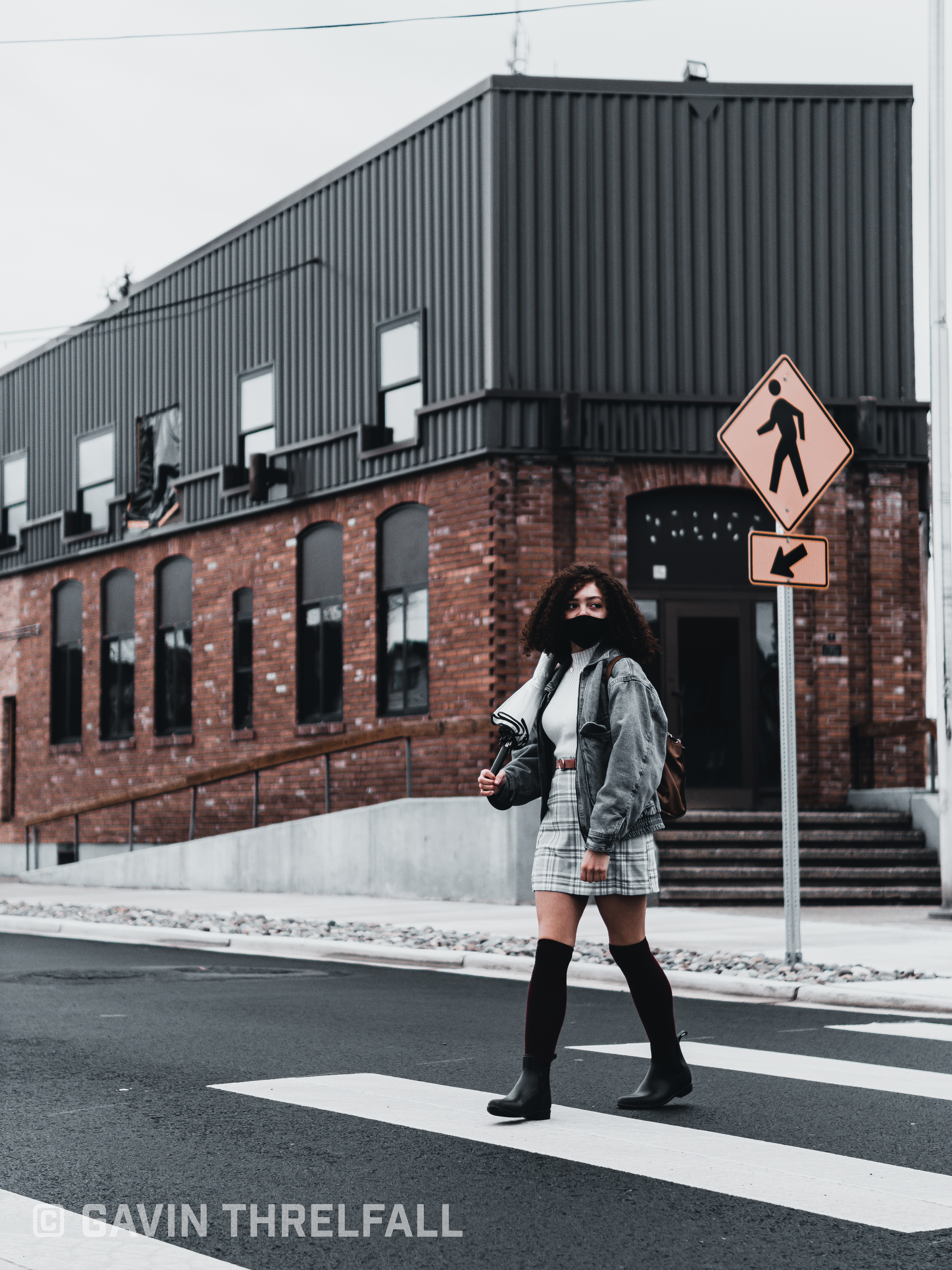 Model walking a crosswalk in front of a brick and metal building