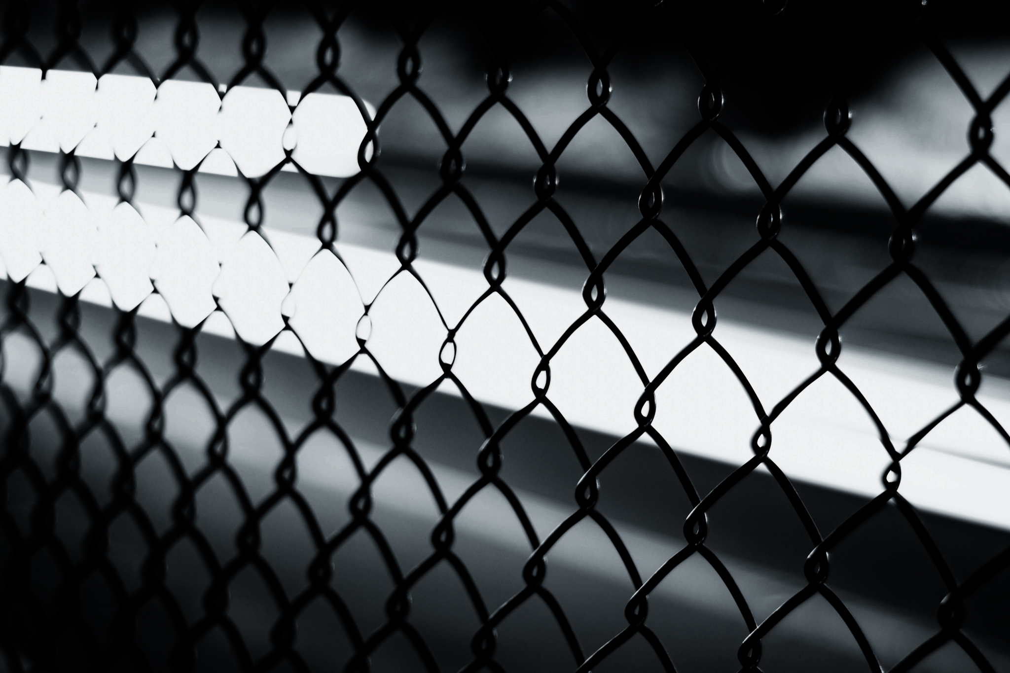 Close-up black and white photo of sunlight striping a chain-link fence