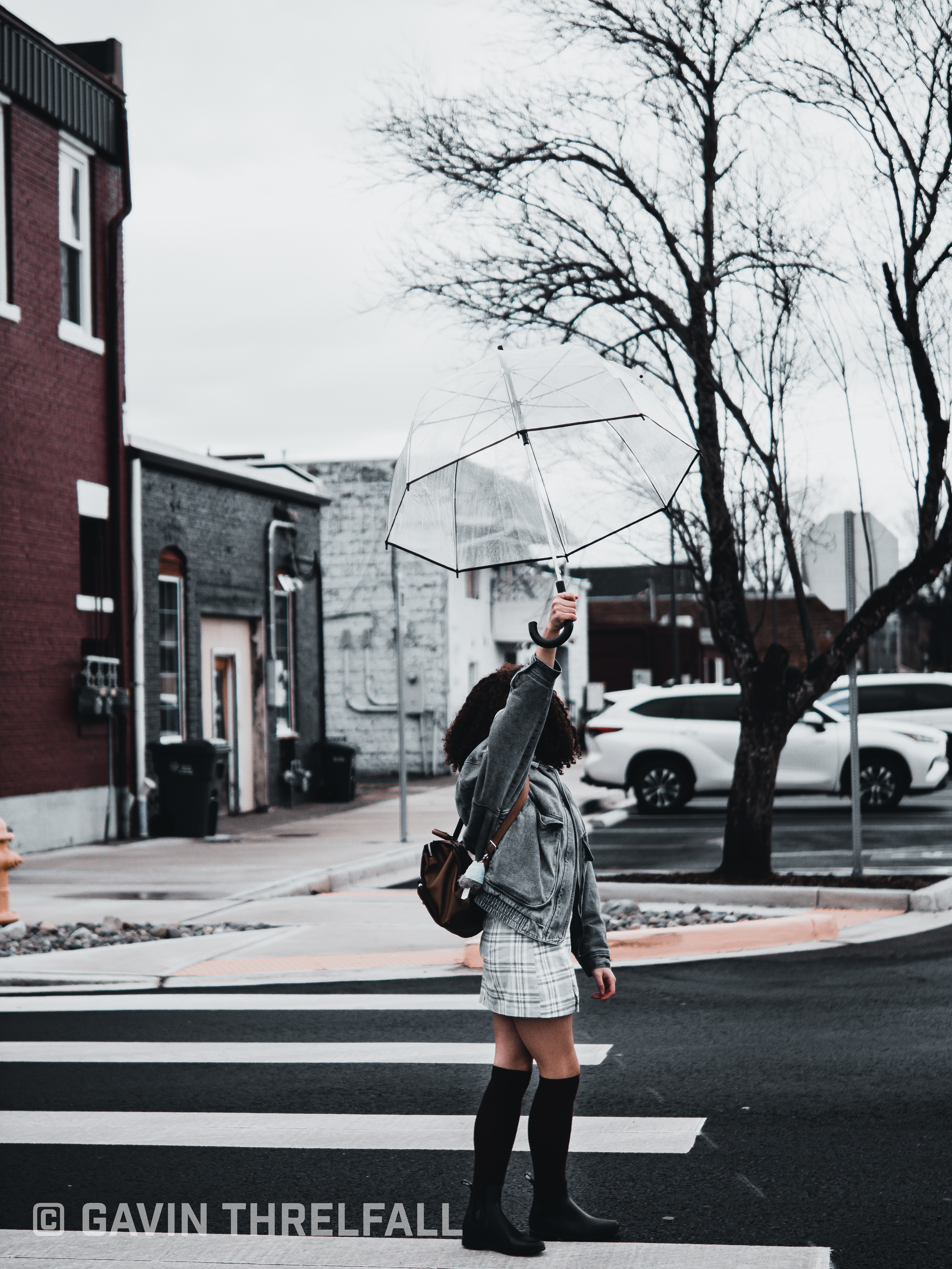 Model holding a clear umbrella while crossing a wet downtown street